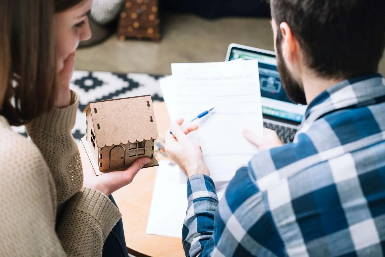 Couple going over home paperwork beside a small wooden house model